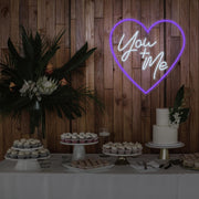 purple you and me neon sign hanging on timber wall above dessert table
