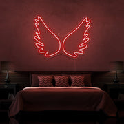 red angel wings neon sign hanging on bedroom wall