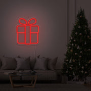 red Christmas present neon sign hanging on lounge room wall next to Christmas tree