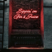 red sippin on gin and juice neon sign hanging on bar wall