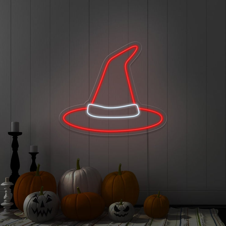 red witch hat neon sign hanging on wall above pumpkins