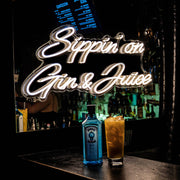 sippin on gin and juice neon sign hanging on bar wall