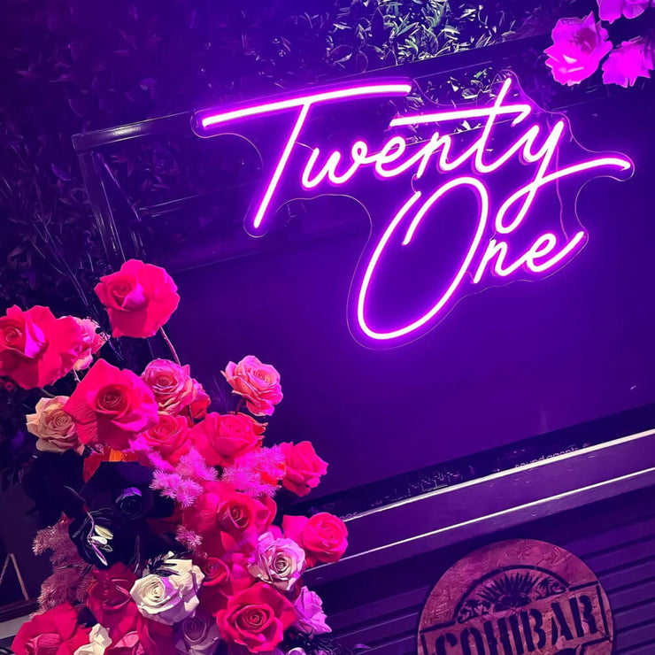 close up of twenty one neon sign hanging on frame with flowers