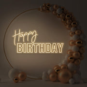 warm white happy birthday neon sign hanging inside gold hoop balloon backdrop