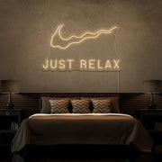 warm white just relax neon sign hanging on bedroom wall