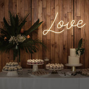 warm white love neon sign hanging on timber wall above dessert table