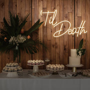 warm white til death neon sign hanging on timber wall above dessert table