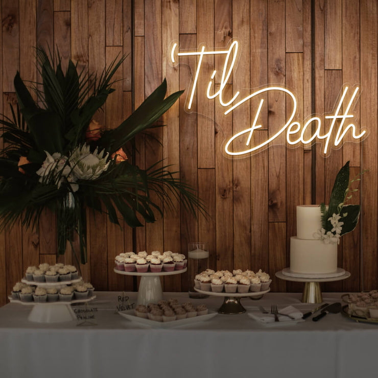warm white til death neon sign hanging on timber wall above dessert table