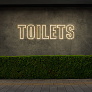 warm white toilets neon sign hanging on outdoor wall