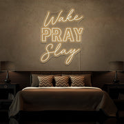 warm white wake pray slay neon sign hanging on bedroom wall