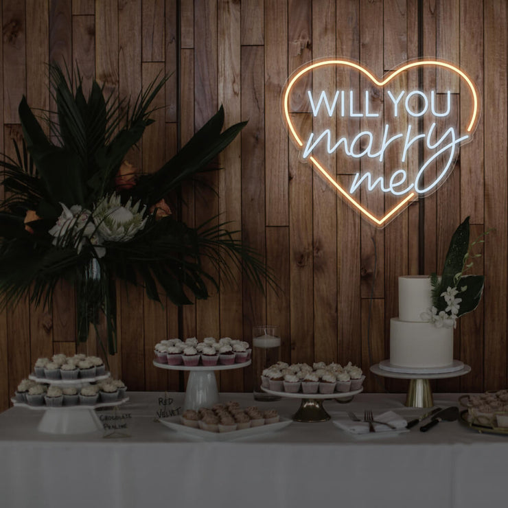 warm white will you marry me heart neon sign hanging on timber wall above dessert table