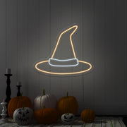 warm white witch hat neon sign hanging on wall above pumpkins