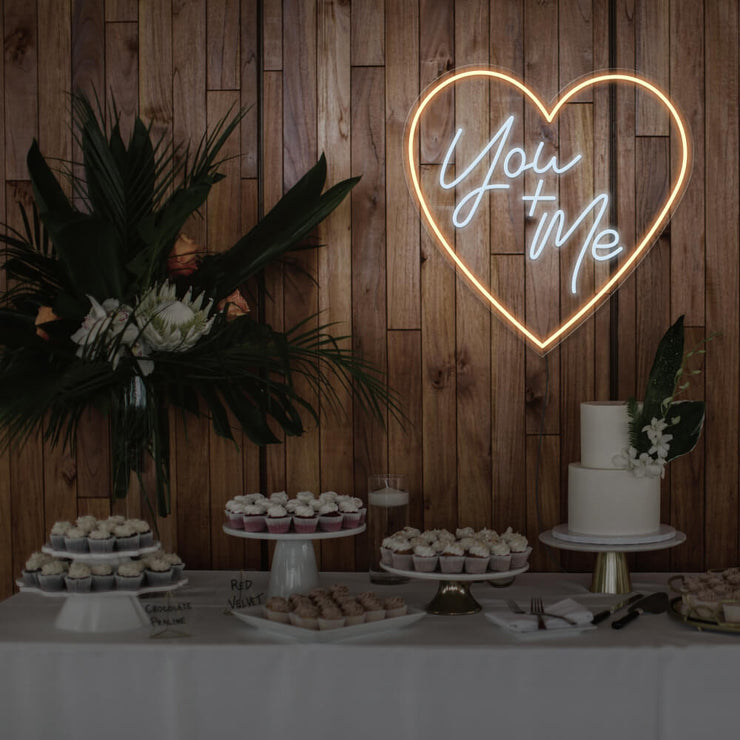 warm white you and me neon sign hanging on timber wall above dessert table