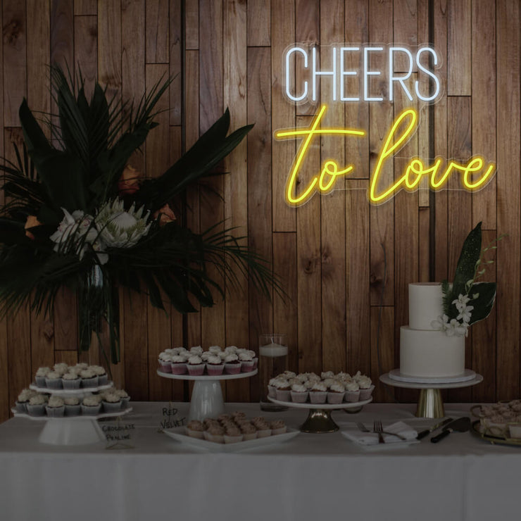 yellow cheers to love neon sign hanging above dessert table
