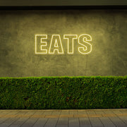 yellow eats neon sign hanging on outside wall