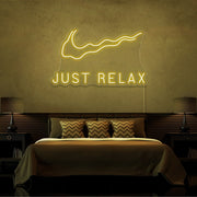 yellow just relax neon sign hanging on bedroom wall