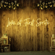 yellow love at first spritz neon sign hanging on timber wall