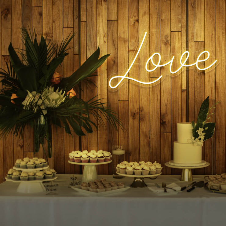 yellow love neon sign hanging on timber wall above dessert table