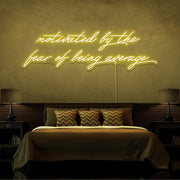 yellow motivated by the fear of being average neon sign hanging on bedroom wall