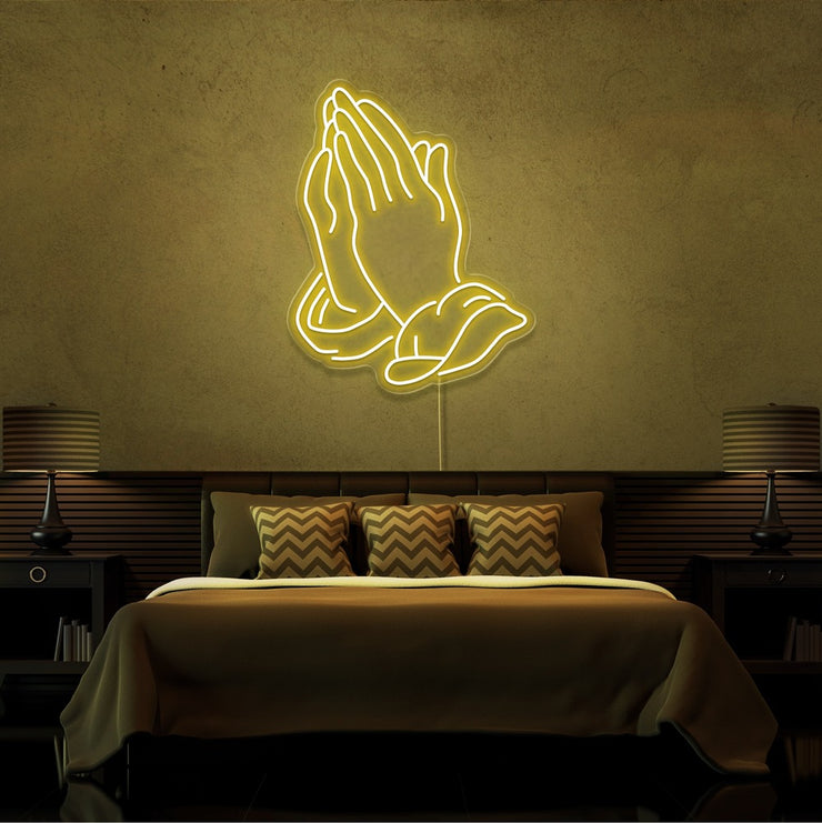 yellow praying hands neon sign hanging on bedroom wall
