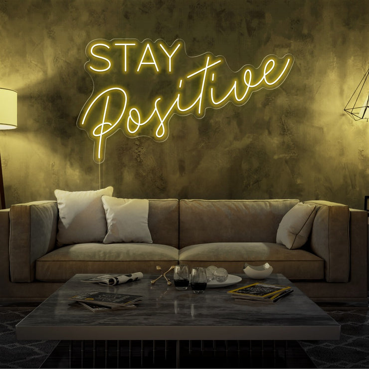 yellow stay positive neon sign hanging on living room wall