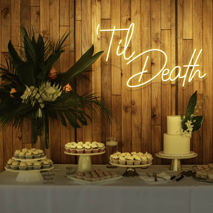 yellow til death neon sign hanging on timber wall above dessert table