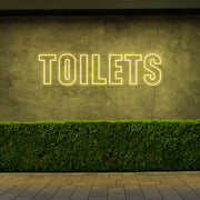 yellow toilets neon sign hanging on outdoor wall