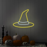 yellow witch hat neon sign hanging on wall above pumpkins